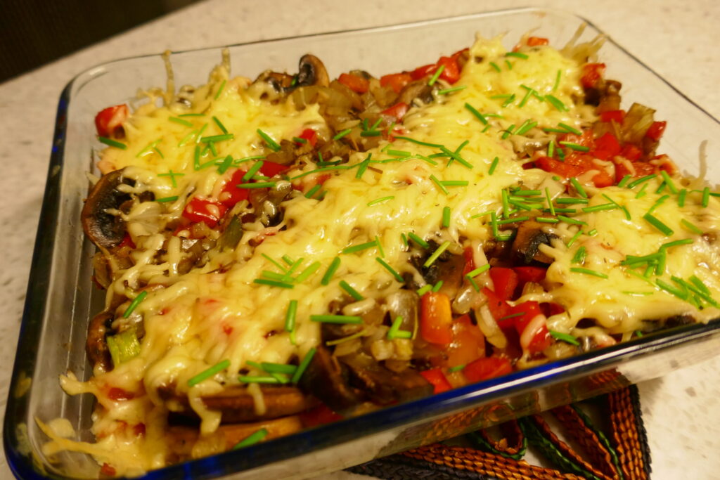 Ovenschotel met geraspte aardappel, champignons, paprika en getopt met kaas