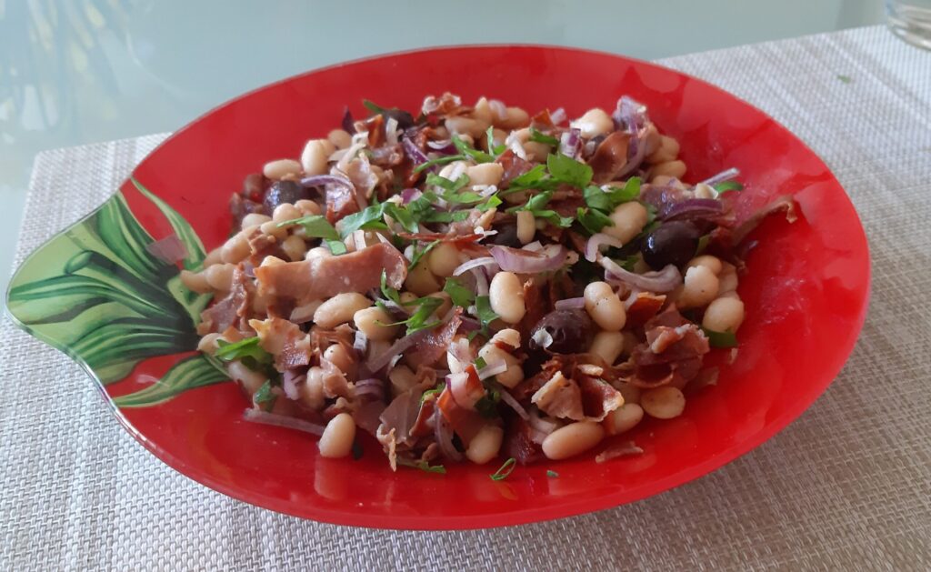 Witte bonensalade met knapperig gebakken Serranoham, gedroogde tomaten, olijven en dunne reepjes rode ui
