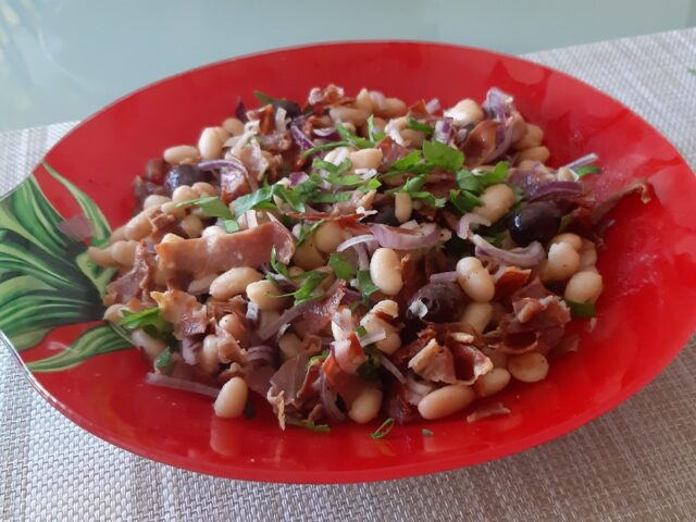 Witte bonensalade met knapperig gebakken Serranoham, gedroogde tomaatjes, Kalamata olijven en dunne reepjes rode ui.