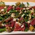 Rucolasalade met carpaccio, olijven, pijnboompitten, Pecorino en kappertjes.