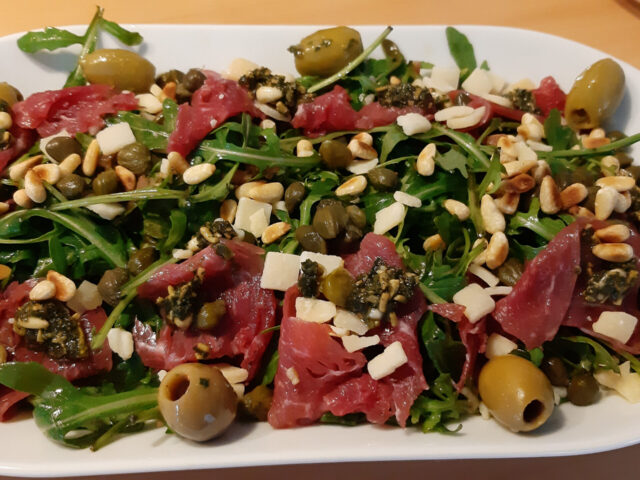 Rucolasalade met carpaccio, olijven, pijnboompitten, Pecorino en kappertjes.